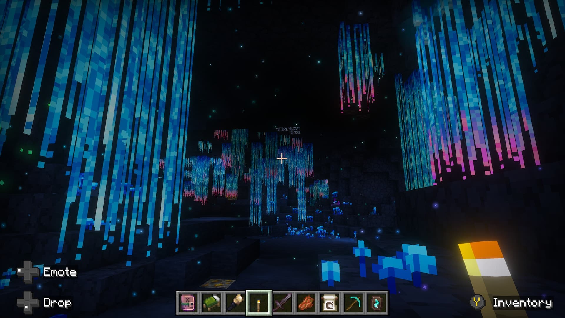 Minecraft player explores a dark cavern illuminated by hanging blue and pink glowing plants and scattered blue vegetation.